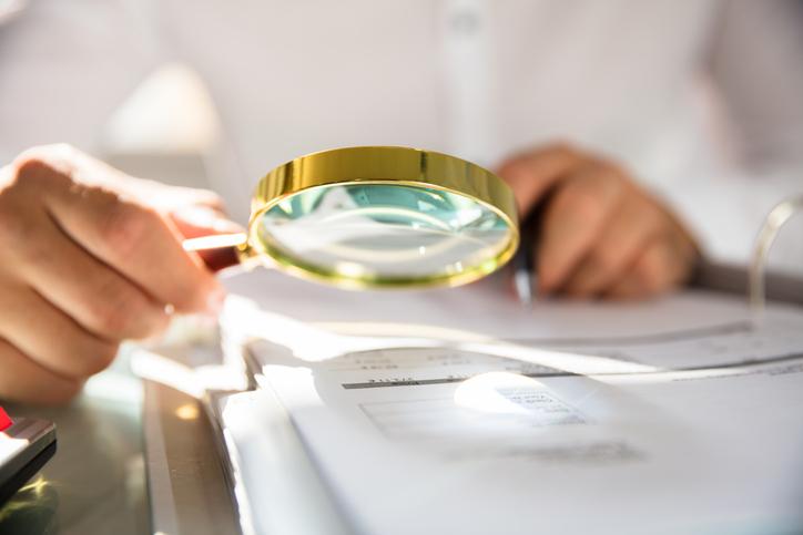 A hand holding a magnifying glass over a stack of papers
