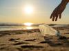Image of someone picking up a plastic bottle from a beach