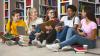 A group of students laugh together while sitting on the floor of a library