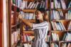 A librarian in a striped dress stacks books on a shelf