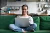 A woman sits on a sofa with a laptop