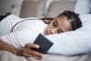 Young Black woman lying on bed looking at phone