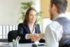 A young woman shakes an interviewer's hand over a table