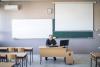 Teacher sitting at his desk in an empty classroom waiting for his students