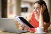 A young woman referring to her notes while stufying at home on her laptop