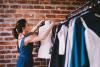 A woman putting a shirt on a mannequin next to clothes rails