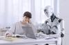 A robot types on a laptop while a bored student slumps beside it