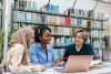 Three female students in library around laptop