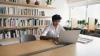 A male researcher writing at his laptop surrounded by shelves of books