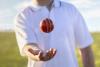 Cricket player tossing ball in hand on pitch