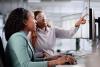 Young black woman looking at screen with help from older black woman, job shadow concept