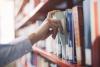 A hand pulling out a book from a library shelf