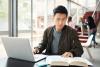 Male Asian student writing on laptop in common area